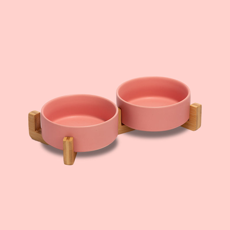 two cute pink pet bowls as a set on the bamboo stand in the pink background