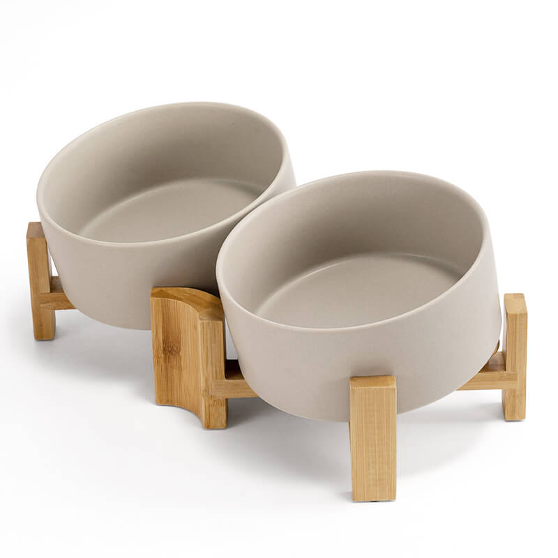 Two grey ceramic dog bowls in a set placed tilted on the bamboo stand