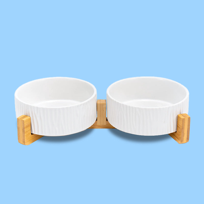 the front view of two white bark-patterned dog bowls on the stand in blue background